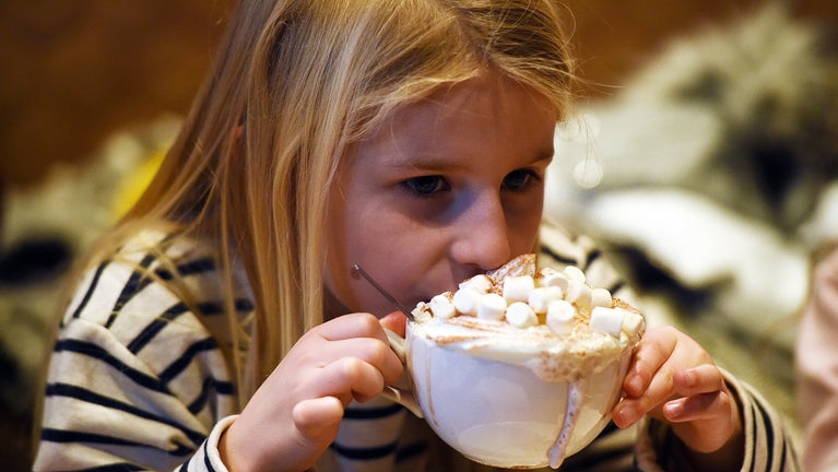 Young girl drinking a large mug of hot chocolate.